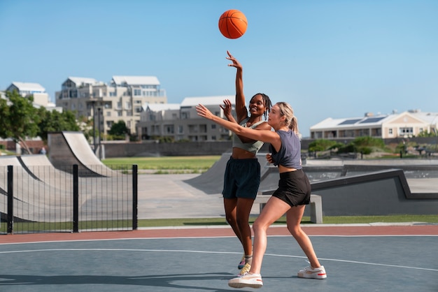 Side view female friends playing basketball