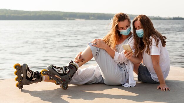 Side view of female friends with medical masks and roller blades by the lake