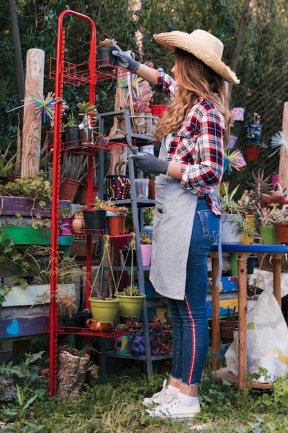 Side view of a female gardener wearing hat arranging the potted plants in the red rack