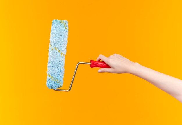 Side view of female hand with paint roller over isolated orange background