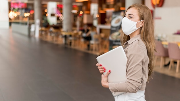 Side view female at mall with laptop wearing mask