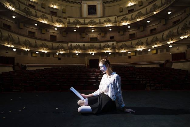 Foto gratuita vista laterale di un mimo femmina seduta sul manoscritto di lettura del palco