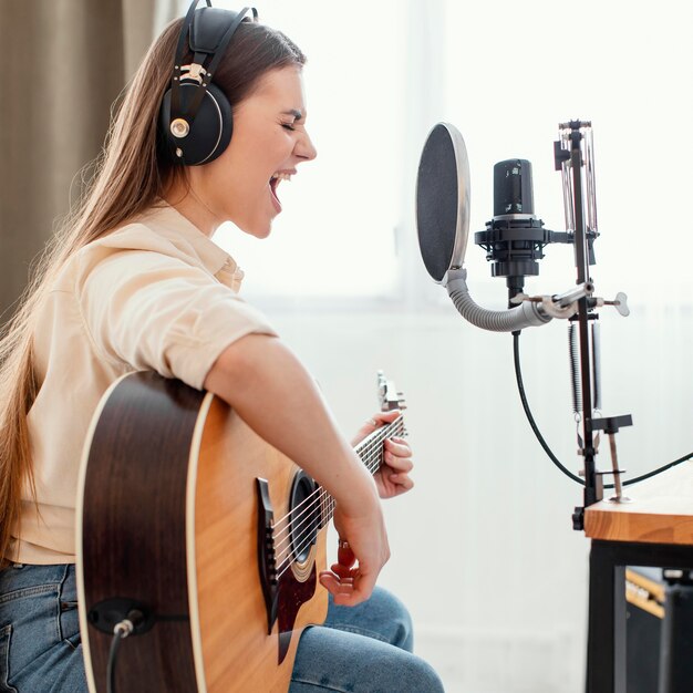 Side view of female musician at home recording song and playing acoustic guitar