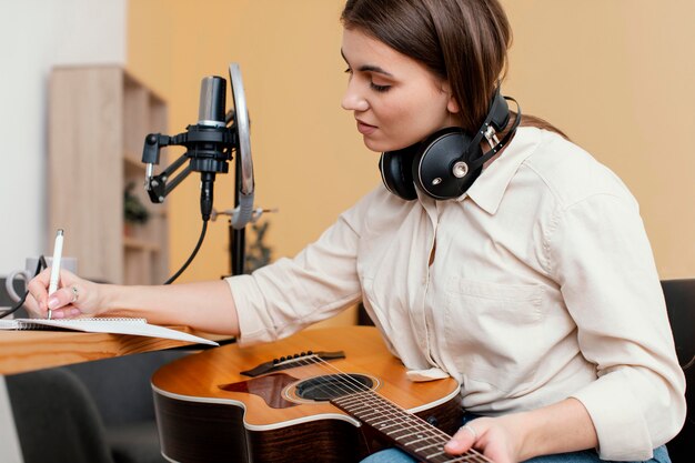 Женщина-музыкант дома пишет песню, играя на акустической гитаре, вид сбоку