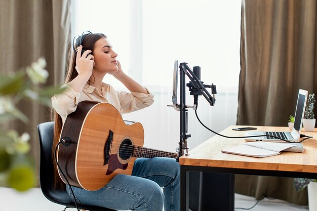 Side view of female musician playing acoustic guitar and preparing to record song at home