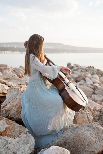 Side view of female musician playing cello on rocks by the sea