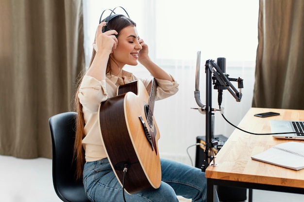 Free photo side view of female musician putting on headphones to record song and play acoustic guitar