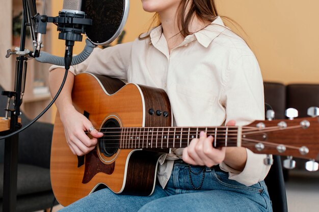 女性ミュージシャンが歌を録音し、自宅でアコースティックギターを演奏する側面図