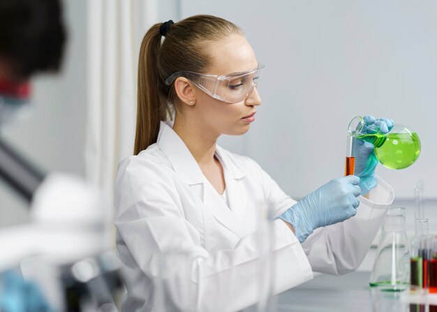 Вид сбоку на женщину-исследователя в лаборатории с пробирками и защитными очками