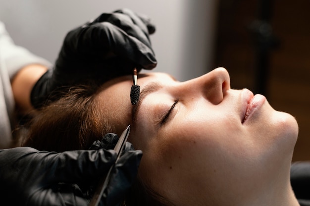 Вид сбоку на женщину-специалиста, делающую лечение бровей для женщины