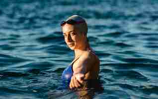 Free photo side view of female swimmer with cap and goggles posing while swimming in water