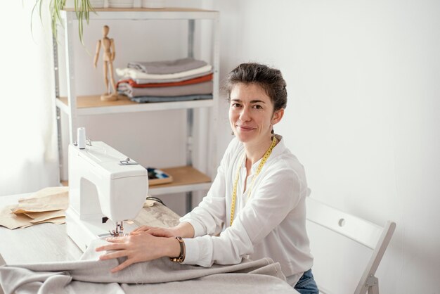 Женский портной, работающий в студии со швейной машиной, вид сбоку
