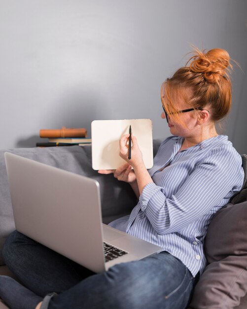 Side view of female teacher on couch holding an online class