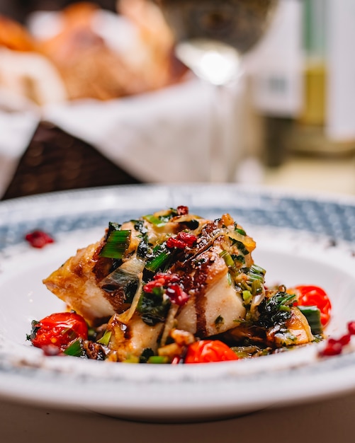 Side view of fish fillet grilled with vegetables served with fresh herbs and sauce on a plate