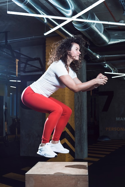 Side view of a fit woman doing jumping squat on wooden box