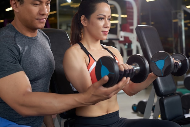 Side view of fit woman working out with personal trainer weightlifting