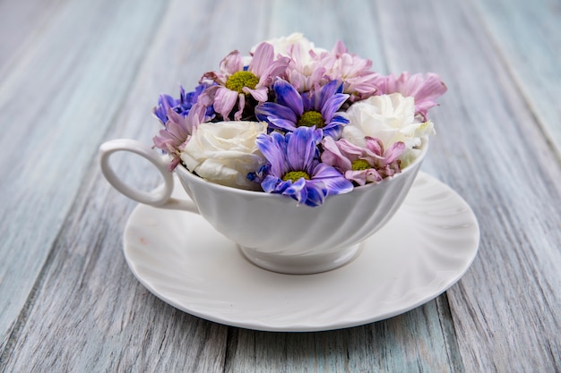 Side view of flowers in cup on saucer on wooden background