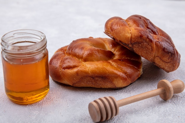 Side view of fluffy and soft buns with honey on a glass jar and wooden honey spoon on a white background