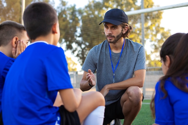 Free photo side view football trainer helping kids