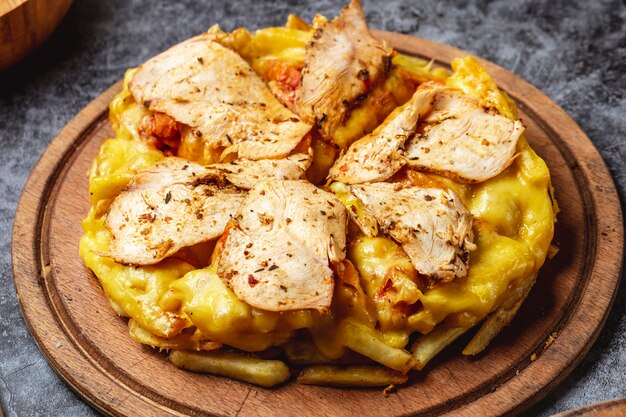 Side view french fries pizza with melted cheese roasted chicken and seasoning on a board