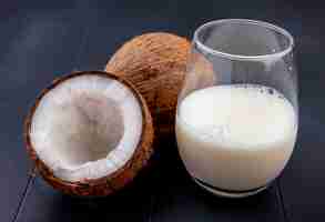 Free photo side view of fresh and brown coconut with a glass of milk on black surface