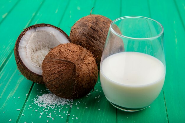 녹색 표면에 우유 한 잔과 신선하고 갈색 코코넛의 측면보기