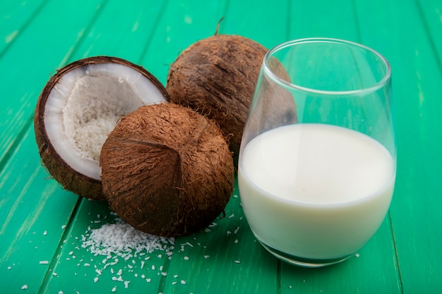 Вид сбоку свежих и коричневых кокосов с стакан молока на зеленой поверхности
