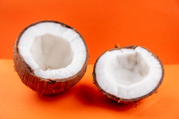 Side view of fresh brown and half coconuts on orange surface