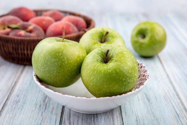 회색 나무 표면에 양동이에 그릇에 복숭아와 사과처럼 신선하고 다채로운 과일의 측면보기