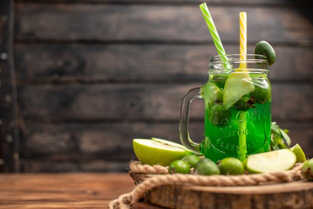 Side view of fresh delicious fruit juice served with apple and feijoas on a wooden cutting board on the left side on a brown table