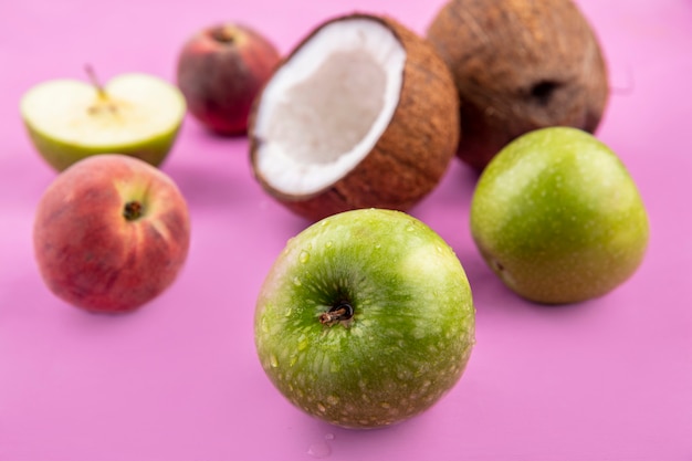Вид сбоку свежих и вкусных фруктов, таких как яблоки, кокосы, изолированные на розовой поверхности