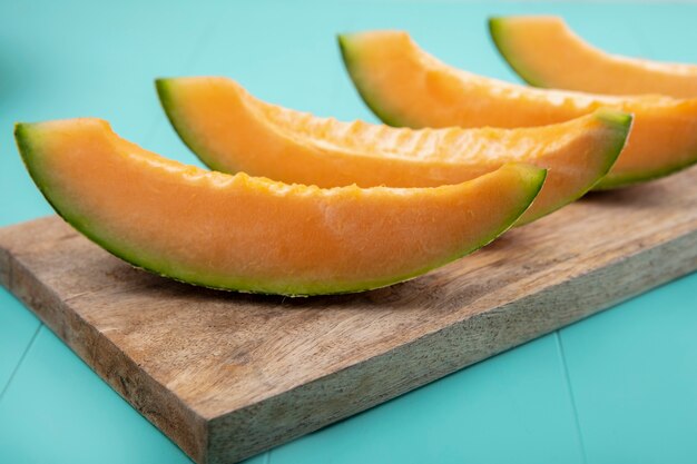 Side view of fresh and delicious melons on a wooden kitchen board on blue surface