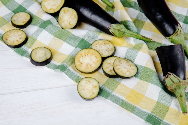 Foto gratuita vista laterale di melanzane fresche con le fette tagliate sul tessuto del plaid su rustico bianco