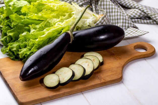 Side view fresh eggplants with slices on a board with lettuce