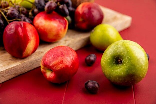 Side view of fresh fruits such as peachgrapeapple on a wooden kitchen board on a red background