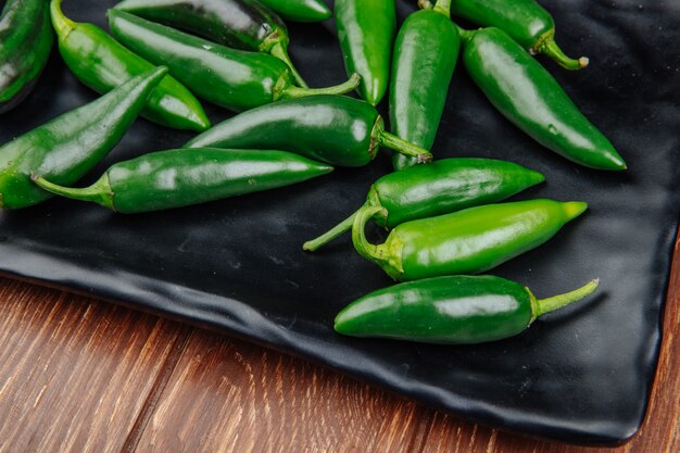 side view of fresh green chili peppers on a black tray on wooden rustic surface