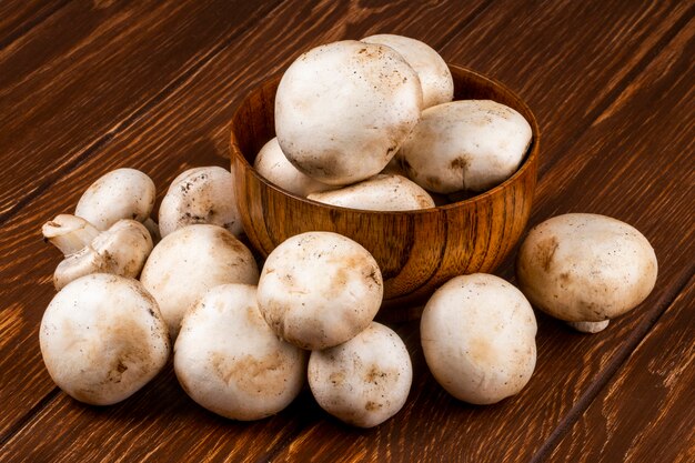 Side view of fresh mushrooms champignon in a bowl on wooden rustic background