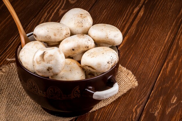 Side view of fresh mushrooms champignon in a pan on wooden rustic background