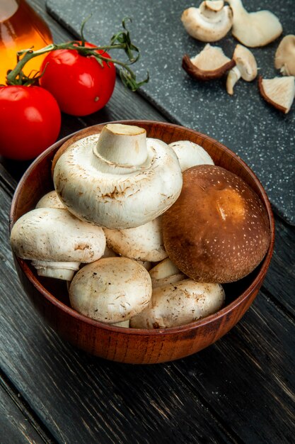 Side view of of fresh mushrooms in a wood bowl and fresh tomatoes on black