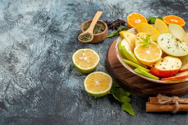 Вид сбоку кусочков свежего натурального яблока на белой тарелке с лимоном на деревянной разделочной доске на темном фоне