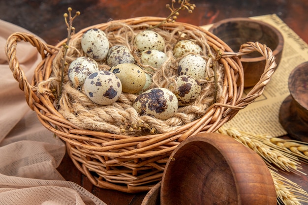 Side view of fresh organic poultry farm eggs in a tissue basket on an old newspaper and nude color towel on wooden bowls on a brown background