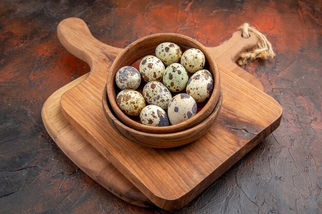Side view of fresh organic poultry farm eggs in a wooden bowl on a cutting board on brown background