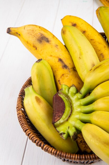 Side view of fresh ripe bananas in a wicker basket on white wood