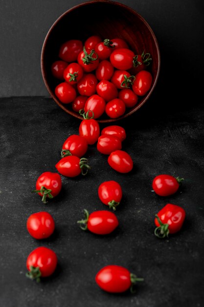 Side view of fresh ripe cherry tomatoes scattered from wooden bowl on black background