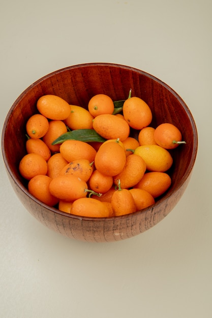 Side view of fresh ripe kumquats in a wood bowl on white