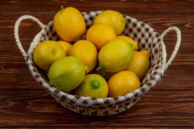 Vista laterale dei limoni maturi freschi in un cestino di vimini bianco su legno