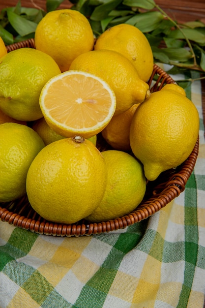 Side view of fresh ripe lemons in a wicker basket with green leaves on plaid fabric