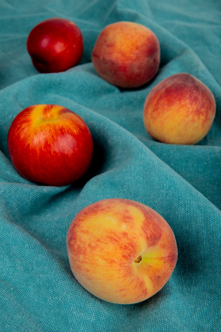 Free Photo side view of fresh ripe nectarines and peaches scattered on blue fabric