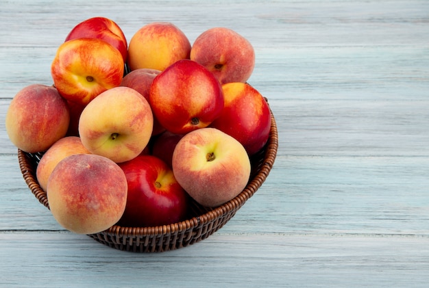 Side view of fresh ripe nectarines and peaches in a wicker basket on  rustic wooden background