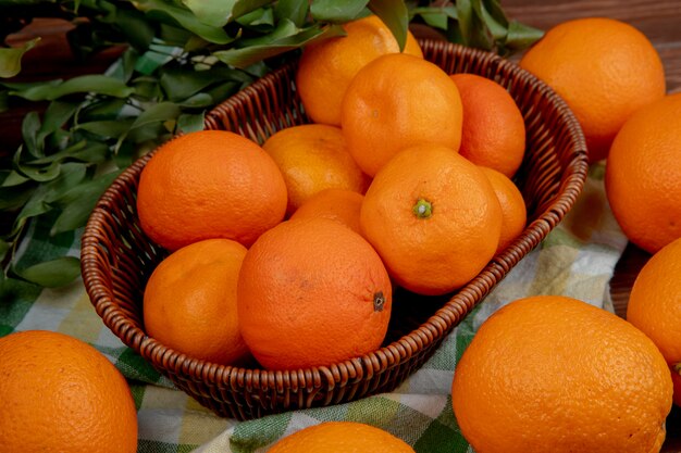 Вид сбоку свежих спелых апельсинов в плетеной корзине на клетчатой скатерти